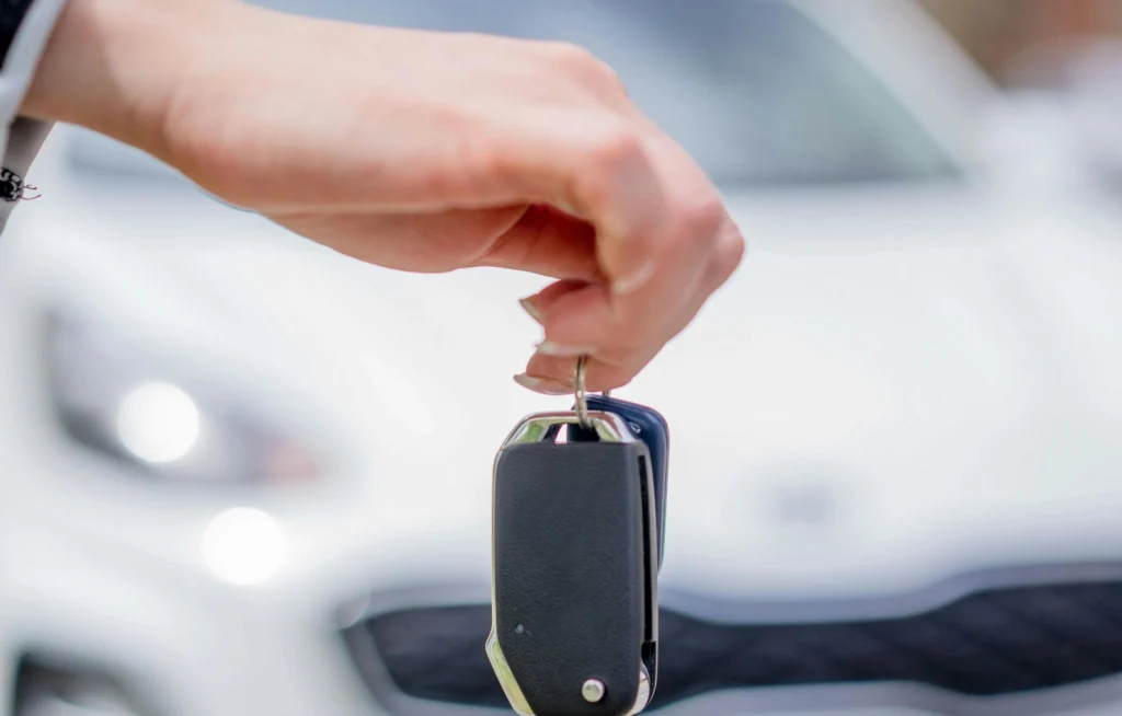 Person holding a car key fob in front of a vehicle