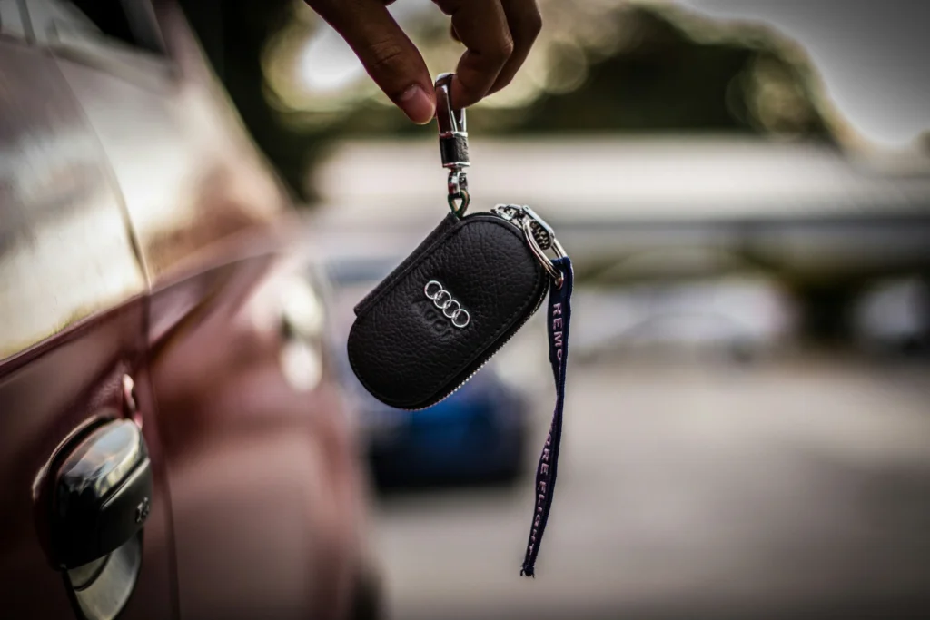 Person holding an Audi car key fob next to a vehicle